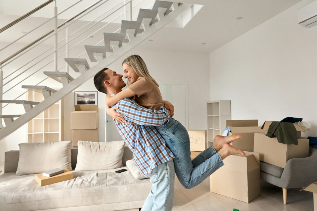 Happy young couple first time home owners hugging in living room on moving day.